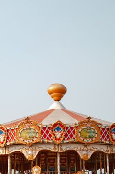 A colorful vintage carousel roof with intricate details against a clear sky, evoking nostalgia.