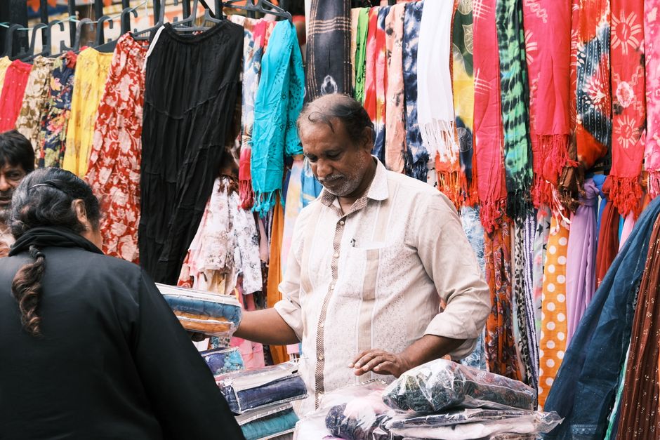 A lively street market in Bengaluru with vibrant fabrics and interactions between vendors and customers.