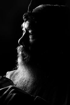 Intriguing black and white portrait of an elderly man with a beard in dark artistic lighting.