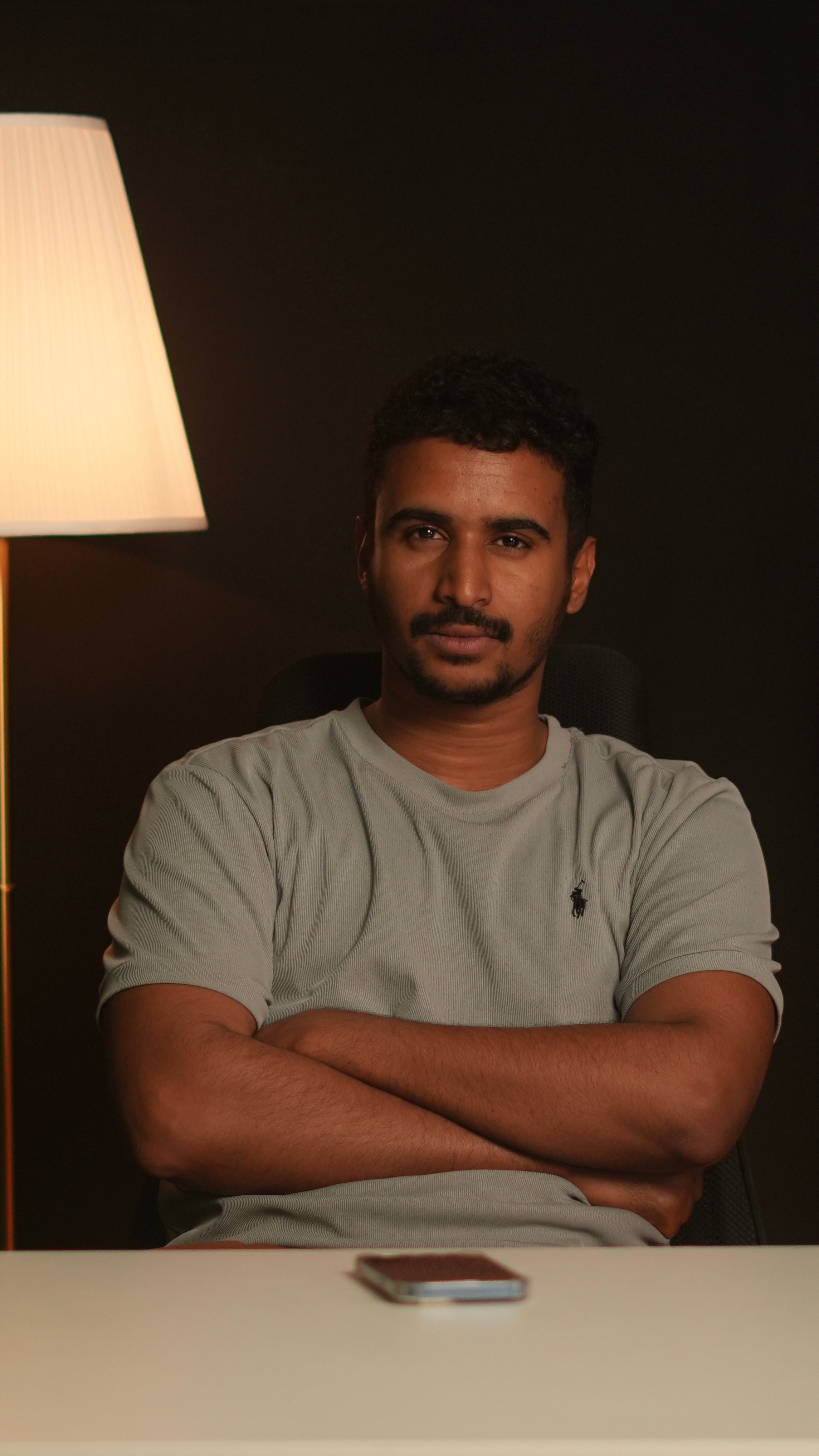 Portrait of a confident man sitting indoors with warm lighting and a lamp.