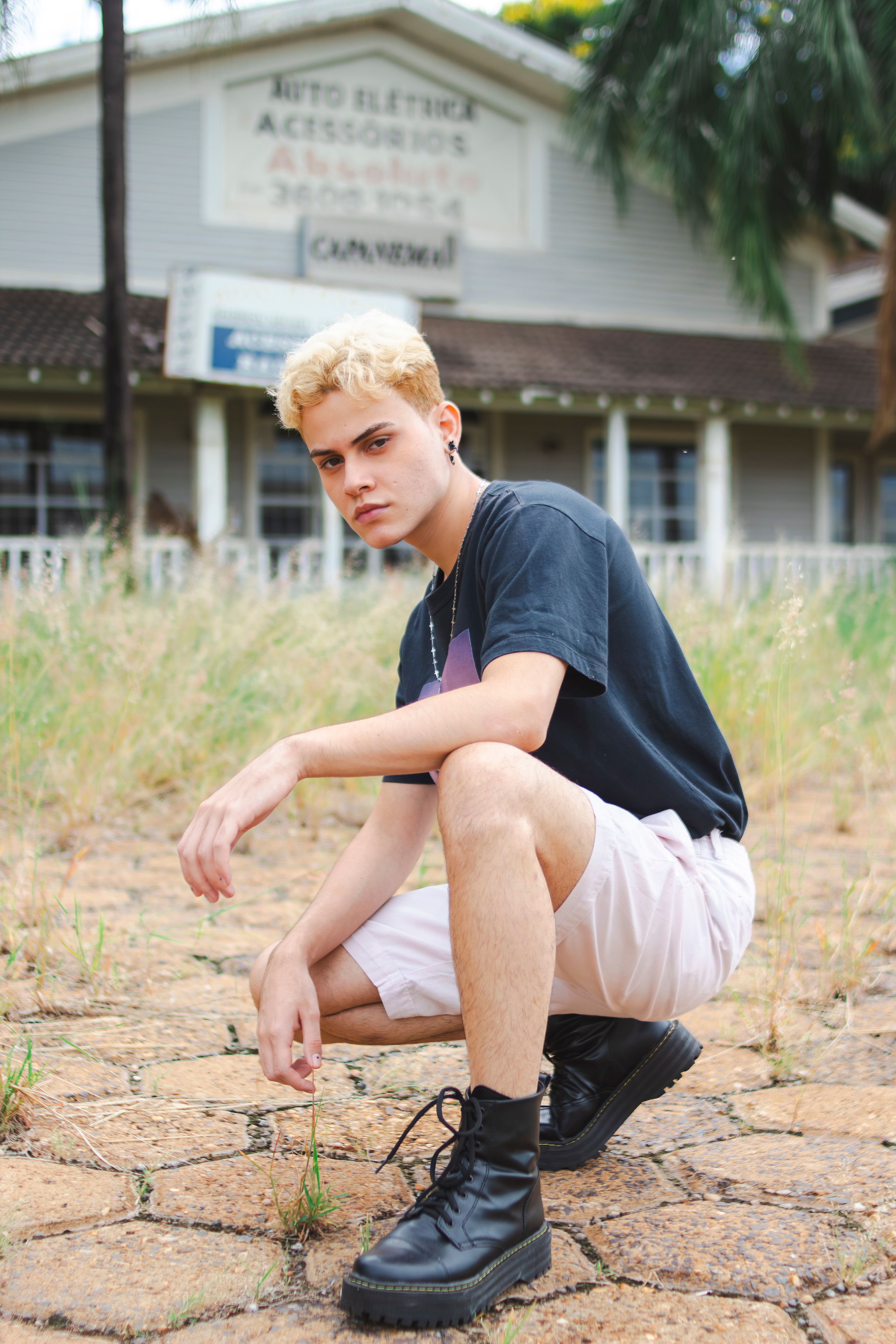 Blonde young man in casual summer attire posing in front of a rustic building.