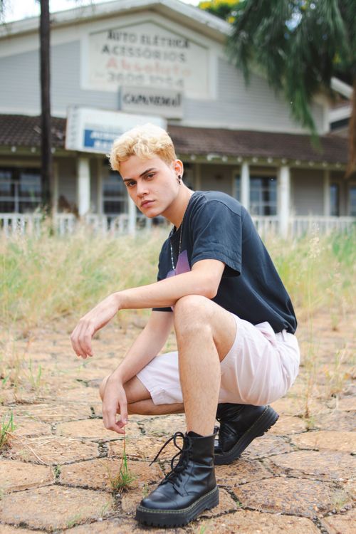 Free Blonde young man in casual summer attire posing in front of a rustic building. Stock Photo