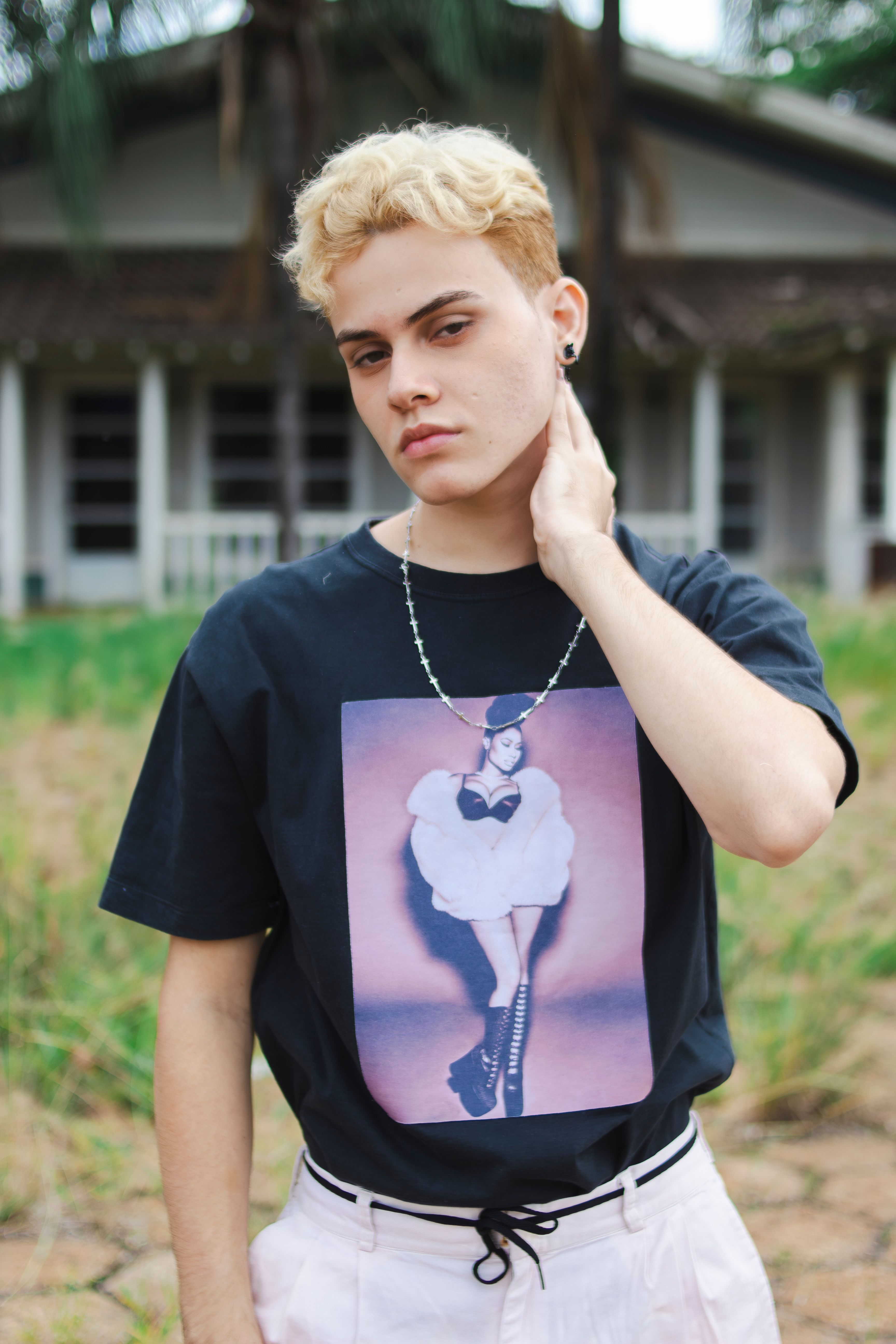 Young adult with blond hair poses outdoors in a fashionable t-shirt.
