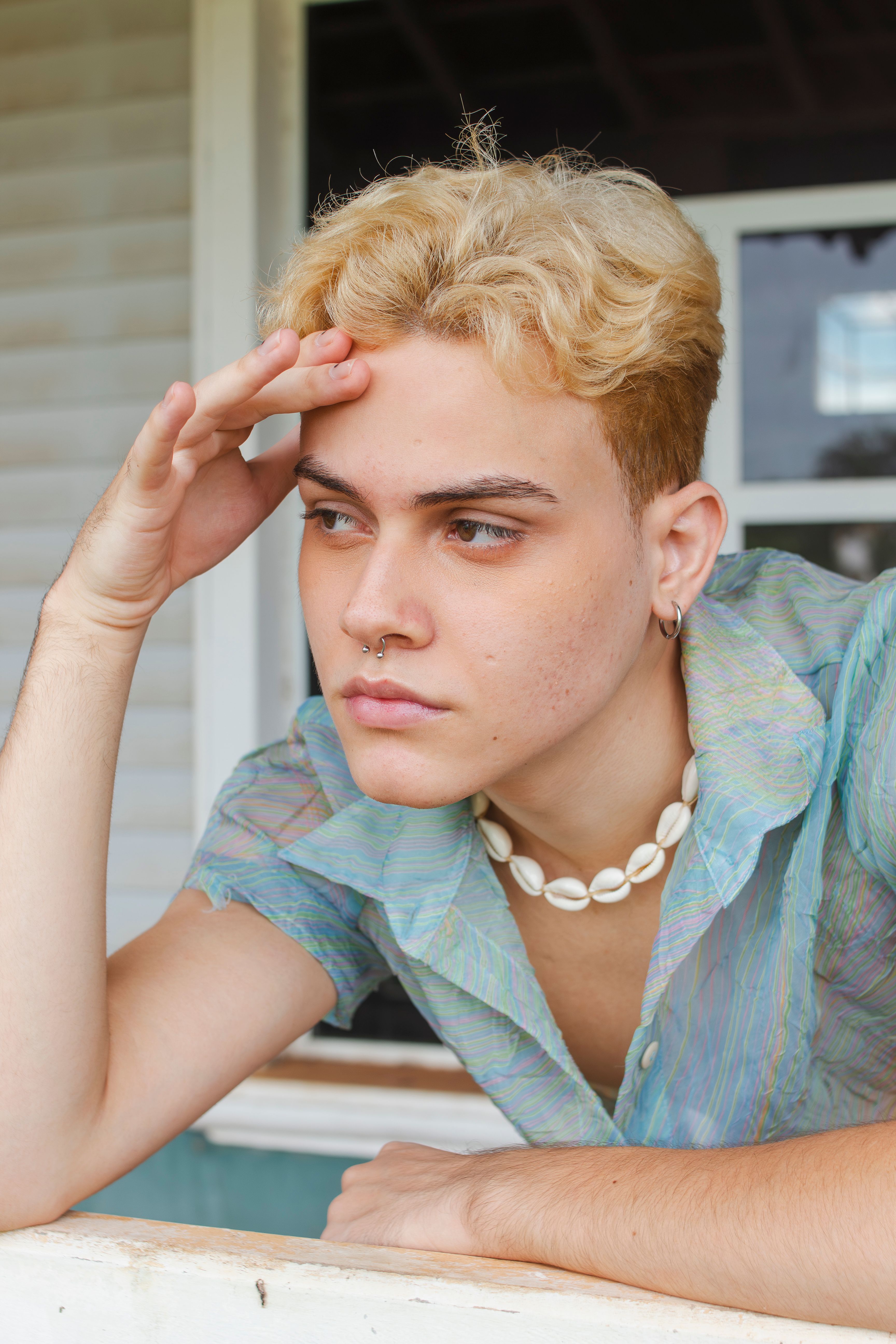 A young adult with blonde hair and casual attire gazing thoughtfully outdoors.