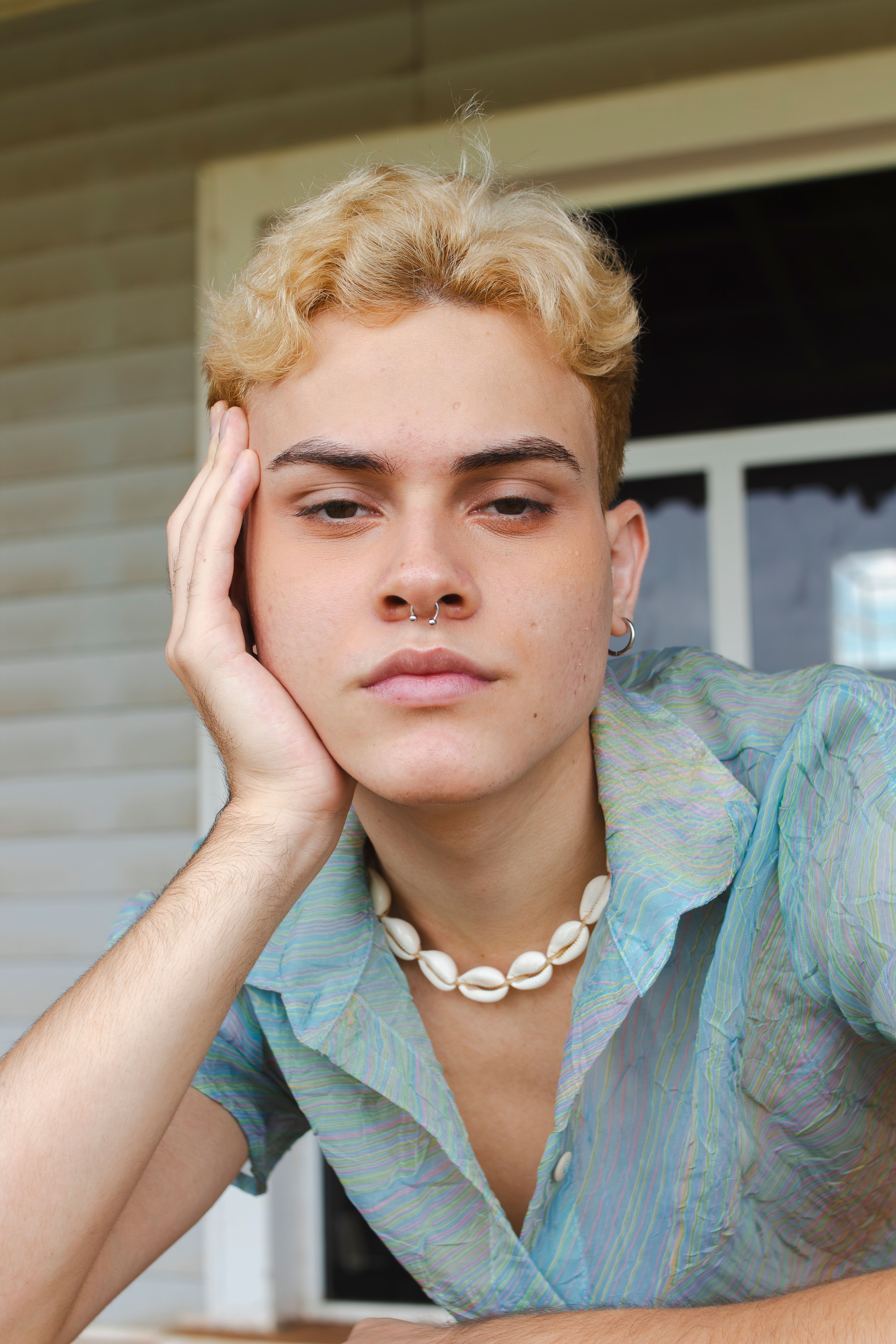 Close-up portrait of a young person with a shell necklace and casual attire, outdoors.