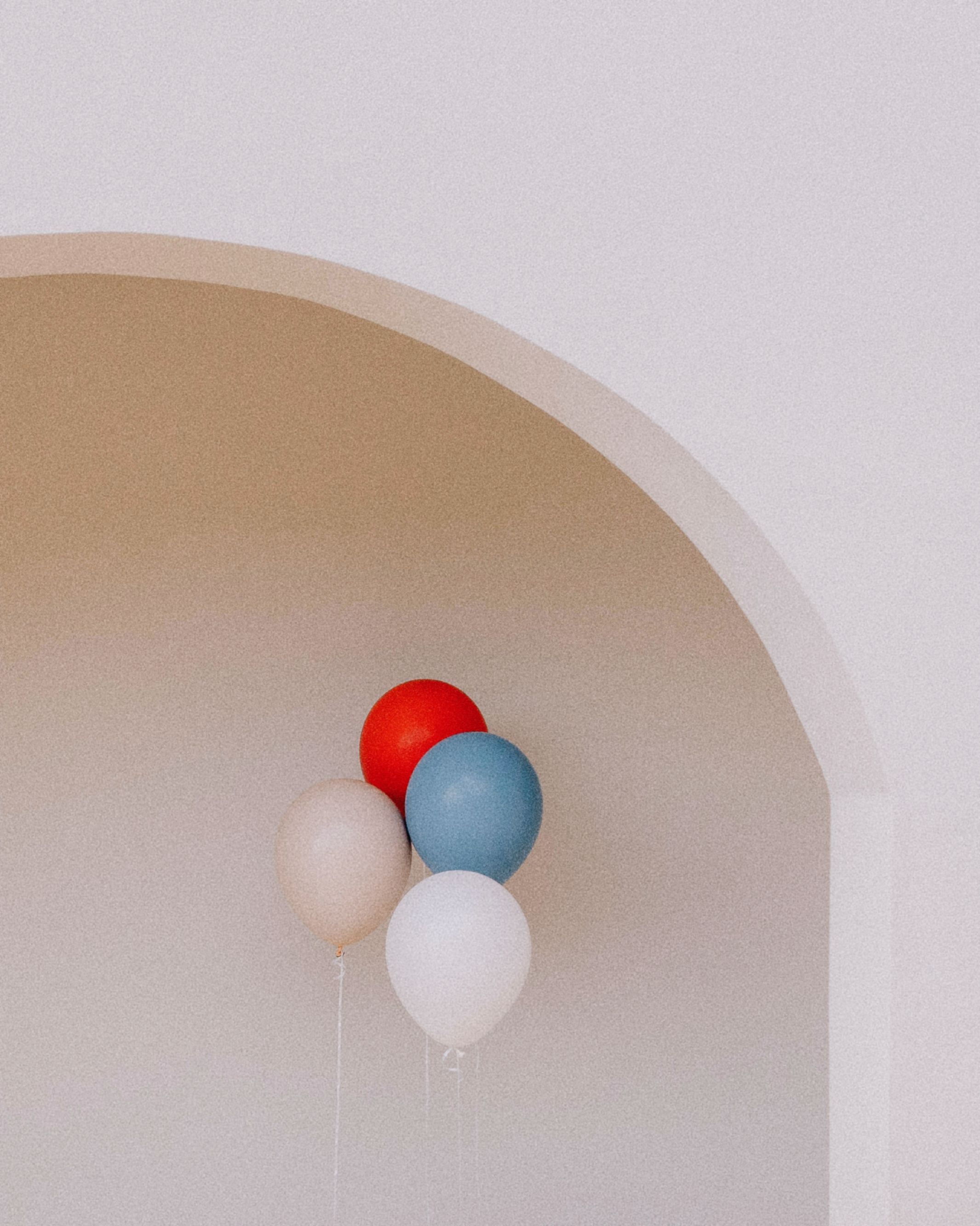 Aesthetic cluster of red, blue, and white balloons against a minimalist arch, creating a whimsical vibe.
