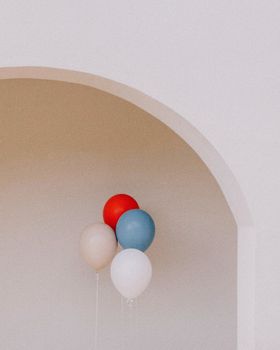 Aesthetic cluster of red, blue, and white balloons against a minimalist arch, creating a whimsical vibe.