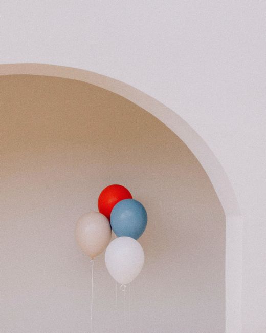 Aesthetic cluster of red, blue, and white balloons against a minimalist arch, creating a whimsical vibe.