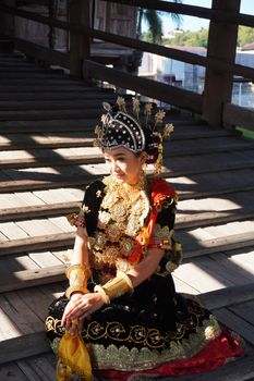 A beautiful Javanese dancer in traditional costume sits on a wooden floor, beaming with elegance. - Fotografer Sidoarjo