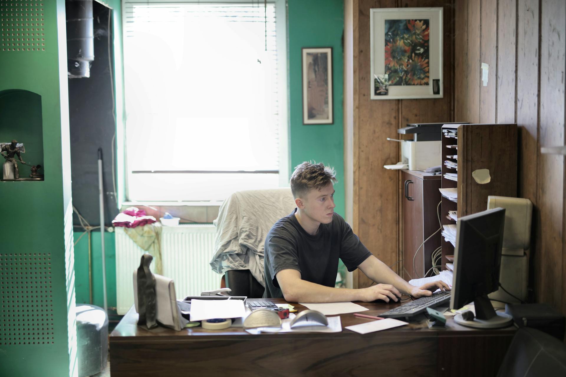 Concentrated male in casual clothes sitting at table and using desktop while working in office