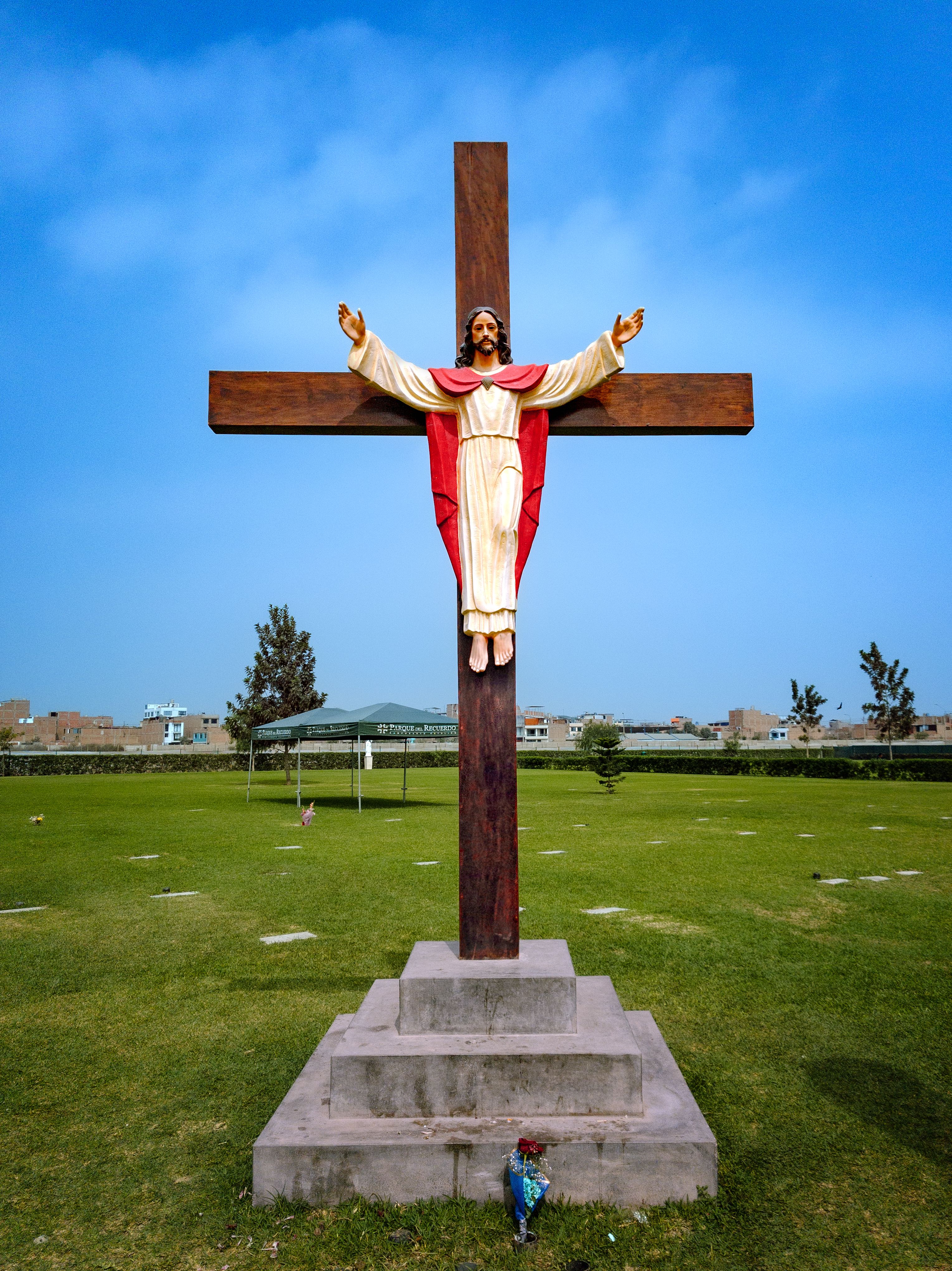 Outdoor statue of Jesus on a cross in a grassy field under a blue sky.