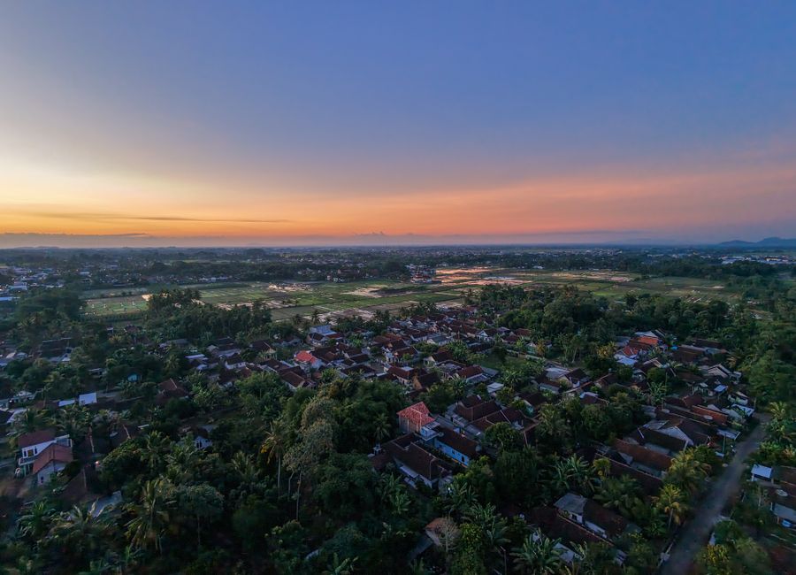 Stunning aerial view of an Indonesian village and rice fields under a colorful sunset sky.