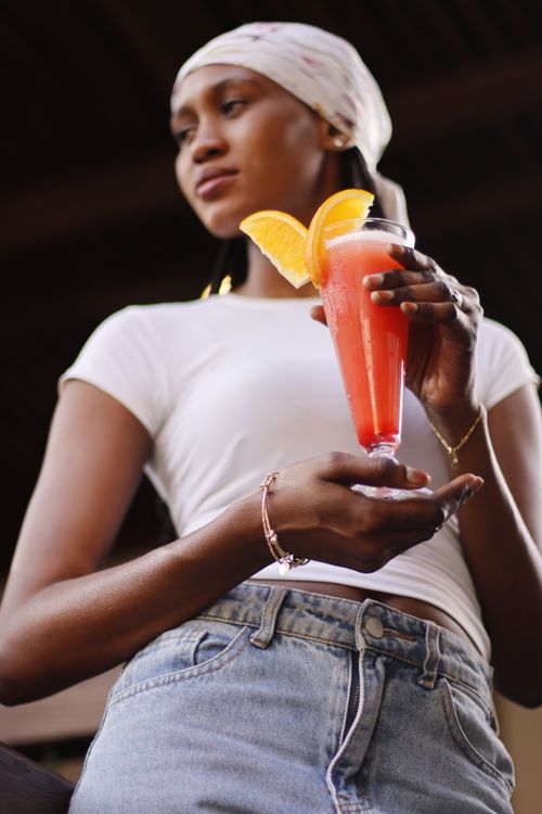 Free Young woman holding a fruity cocktail with orange slice garnish, enjoying a relaxed day outdoors. Stock Photo