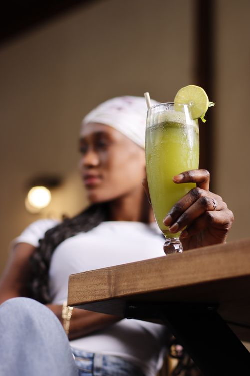 Free A woman relaxes indoors holding a vibrant green drink with a lime garnish, embodying leisure and freshness. Stock Photo