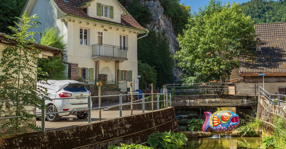 Picturesque Swiss village scene featuring a colorful fish sculpture by a stream.