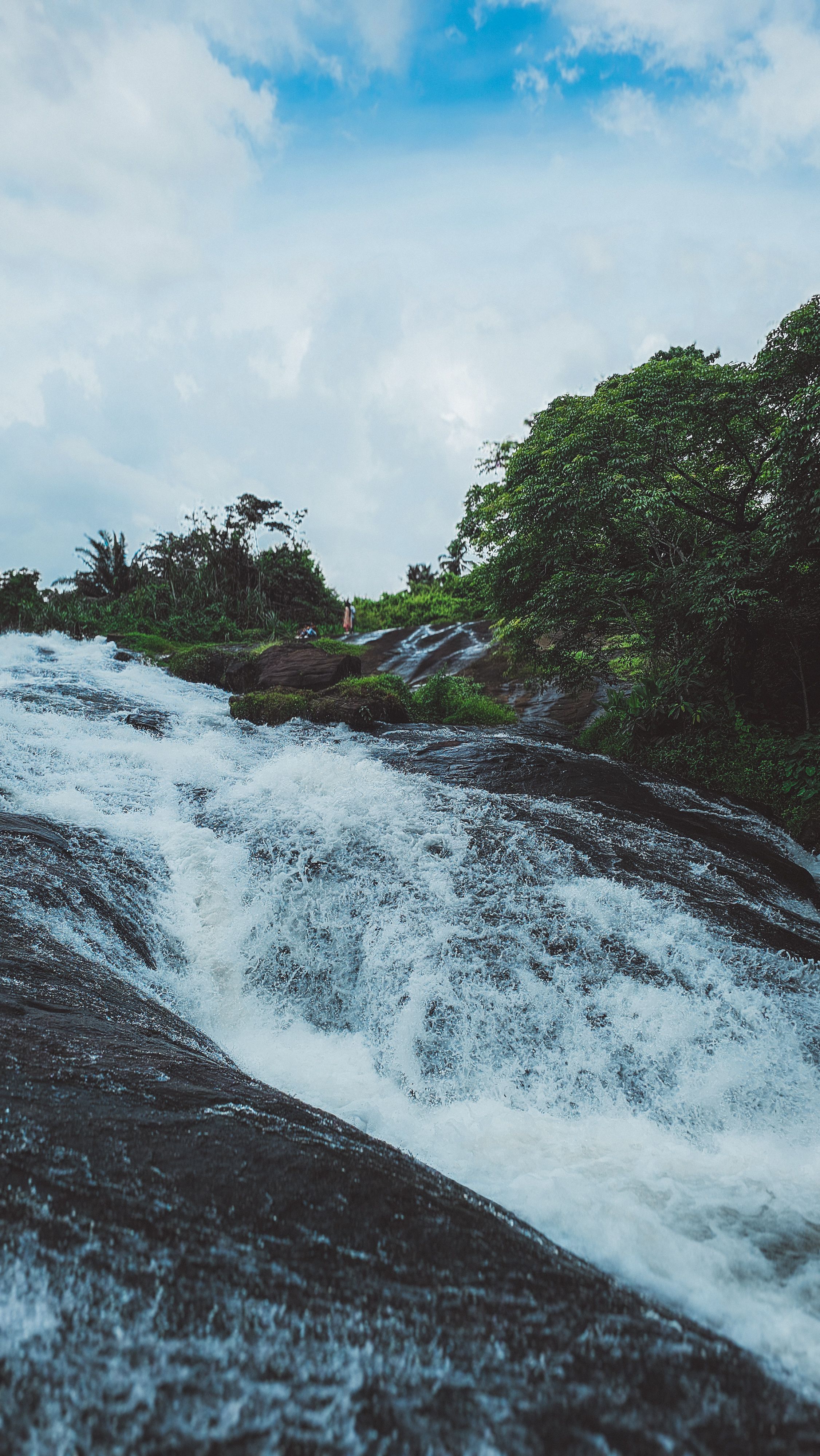 Pristine waterfall cascading through a lush, tropical forest under a bright blue sky.