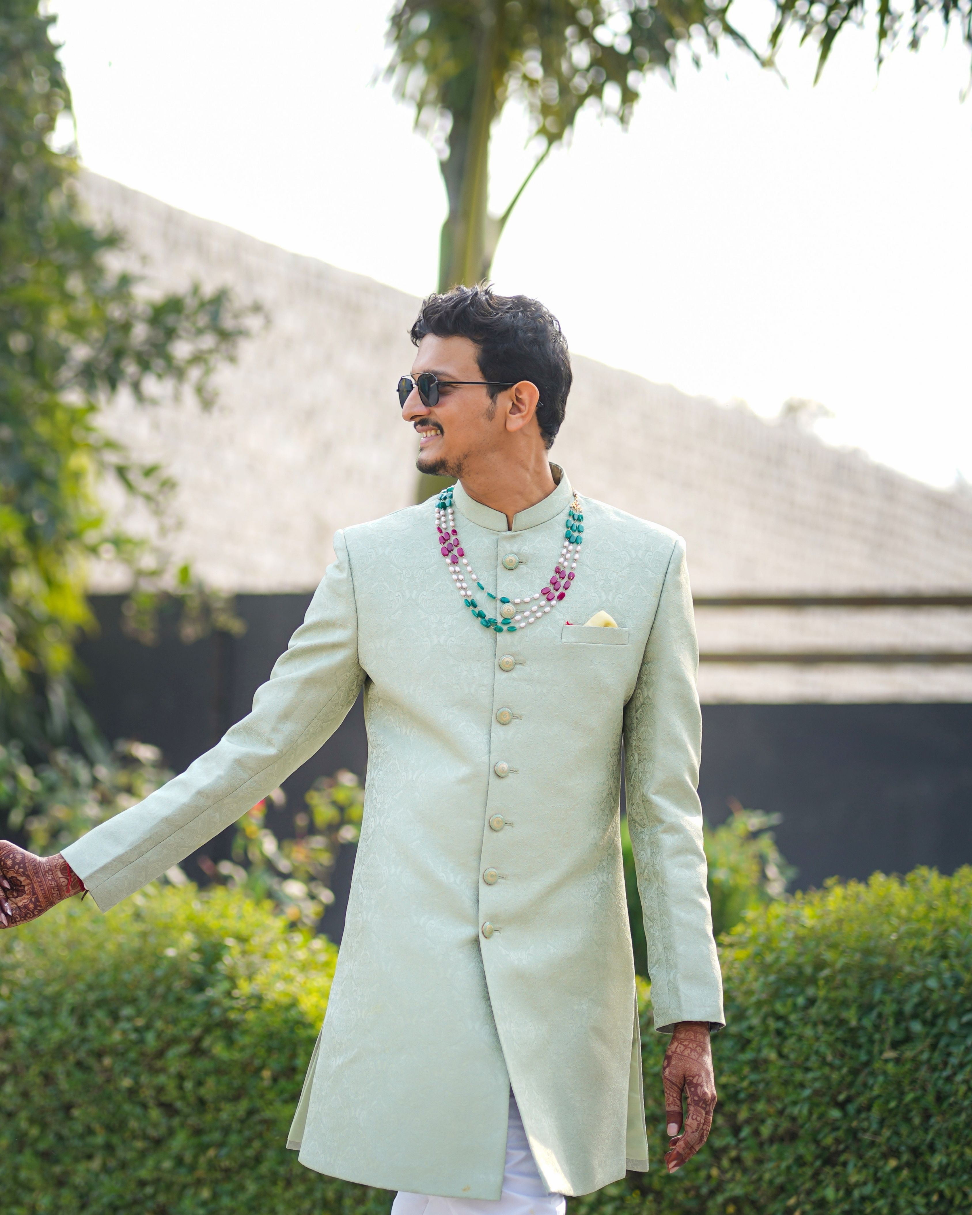 A stylish groom poses in a traditional attire outdoors during a sunny day in Rajasthan, India.