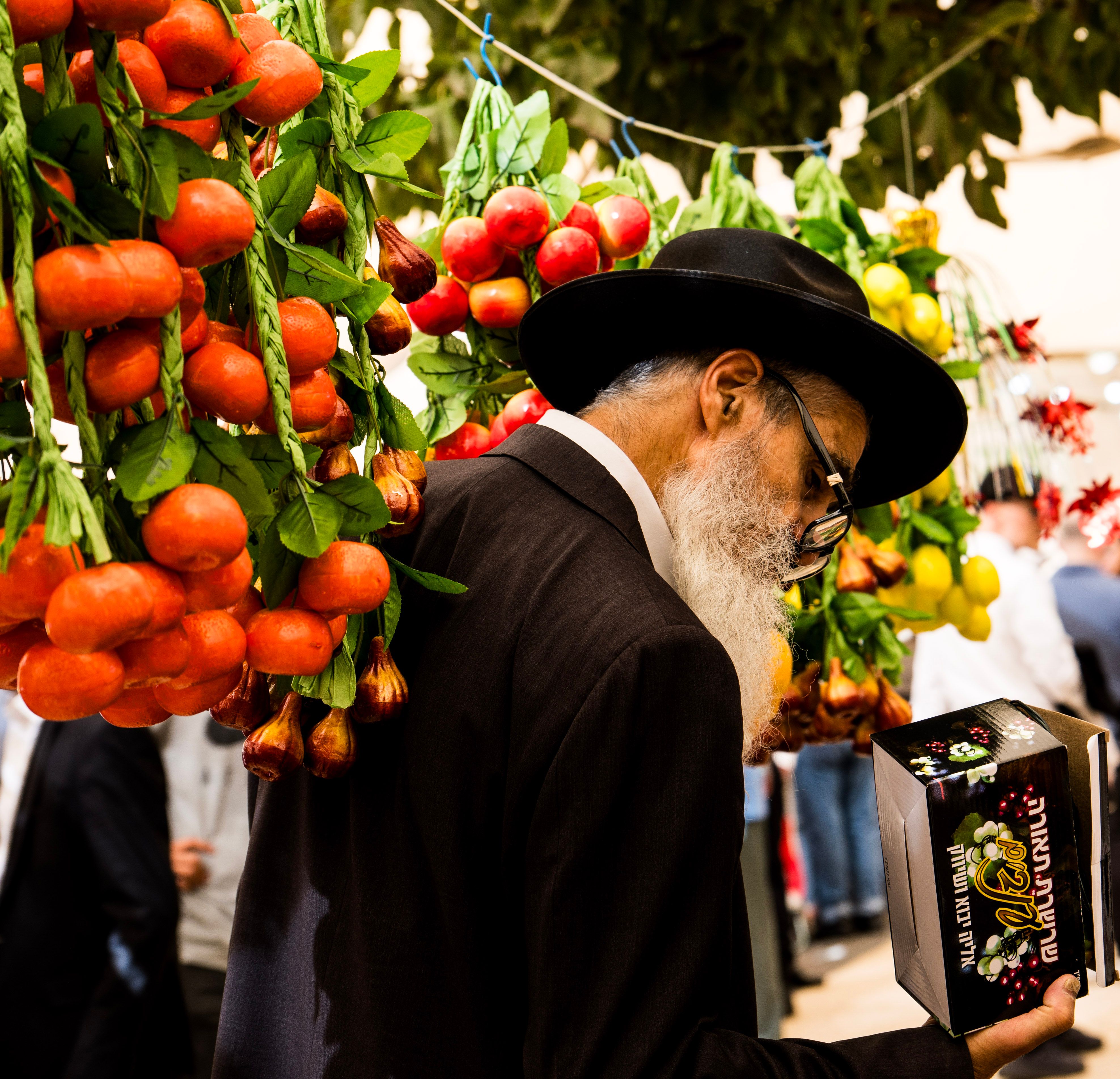 A man examines items in a vibrant market display with hanging fruit decorations.