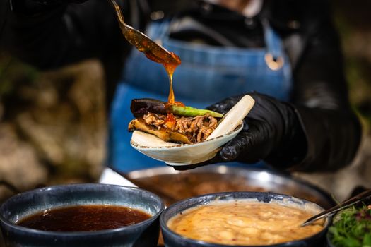 Close-up of street vendor garnishing a taco with sauce, showcasing vibrant street food culture.