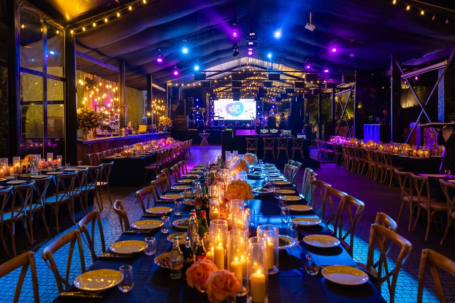 Long tables set with candles at an evening event, warm light pooling across the linen.