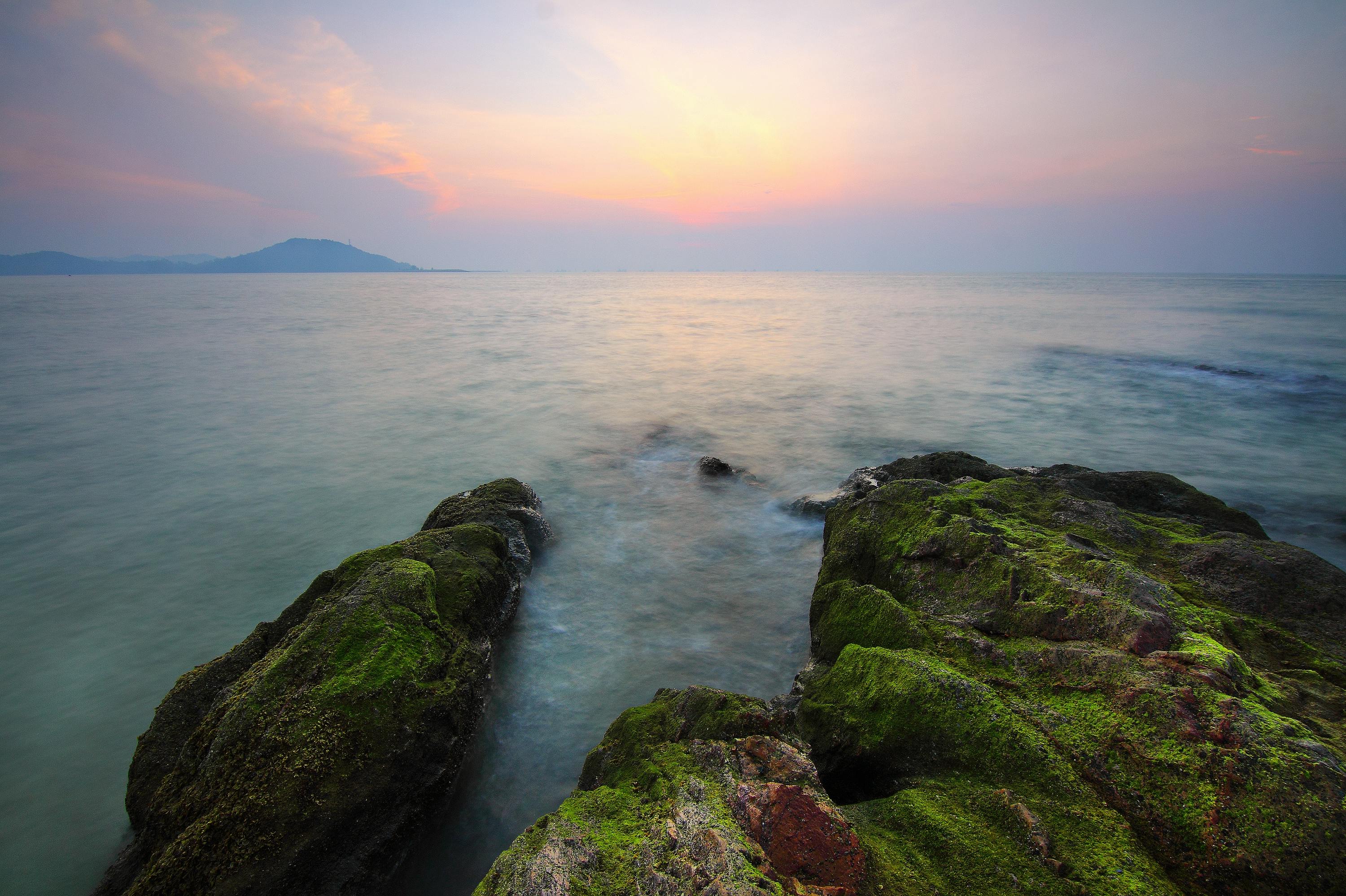 前景是长满青苔的岩石，背景是宁静的山脉轮廓，构成了一幅令人惊叹的黎明海景