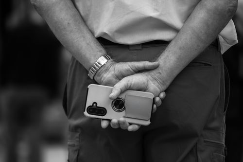Free A candid black and white shot of a person waiting, holding a smartphone behind their back. Stock Photo