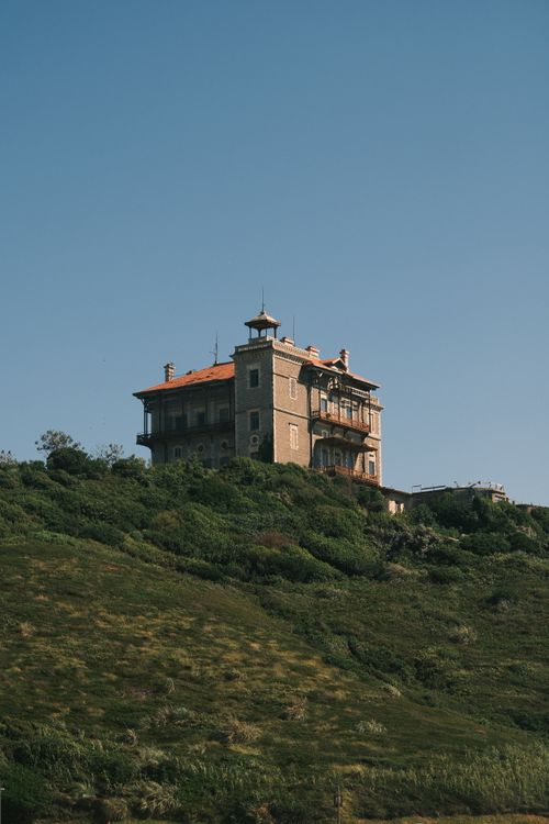 Free A picturesque historic mansion sits atop a lush green hillside under a clear blue sky. Stock Photo