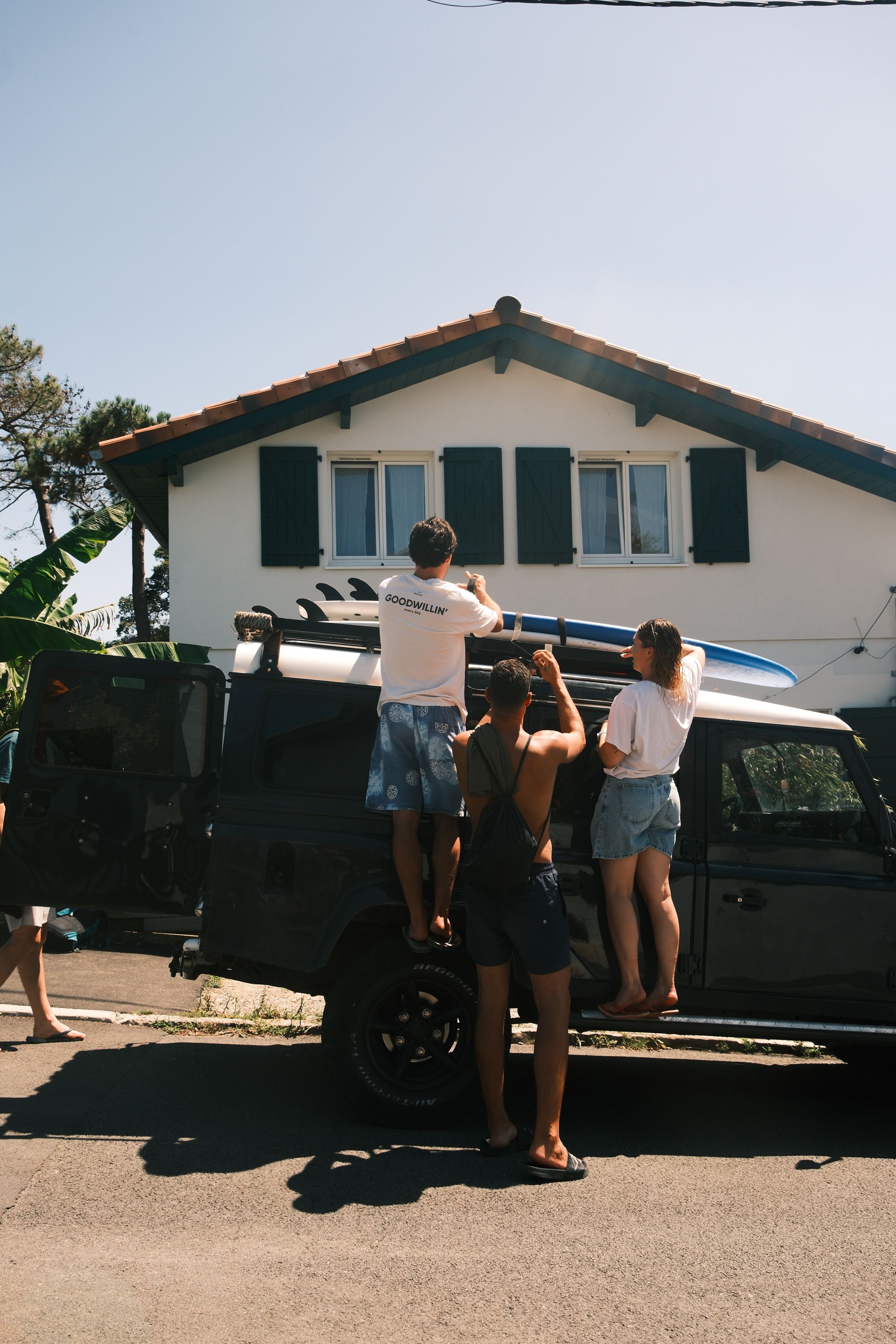Friends loading surfboards onto a car on a sunny New Zealand street