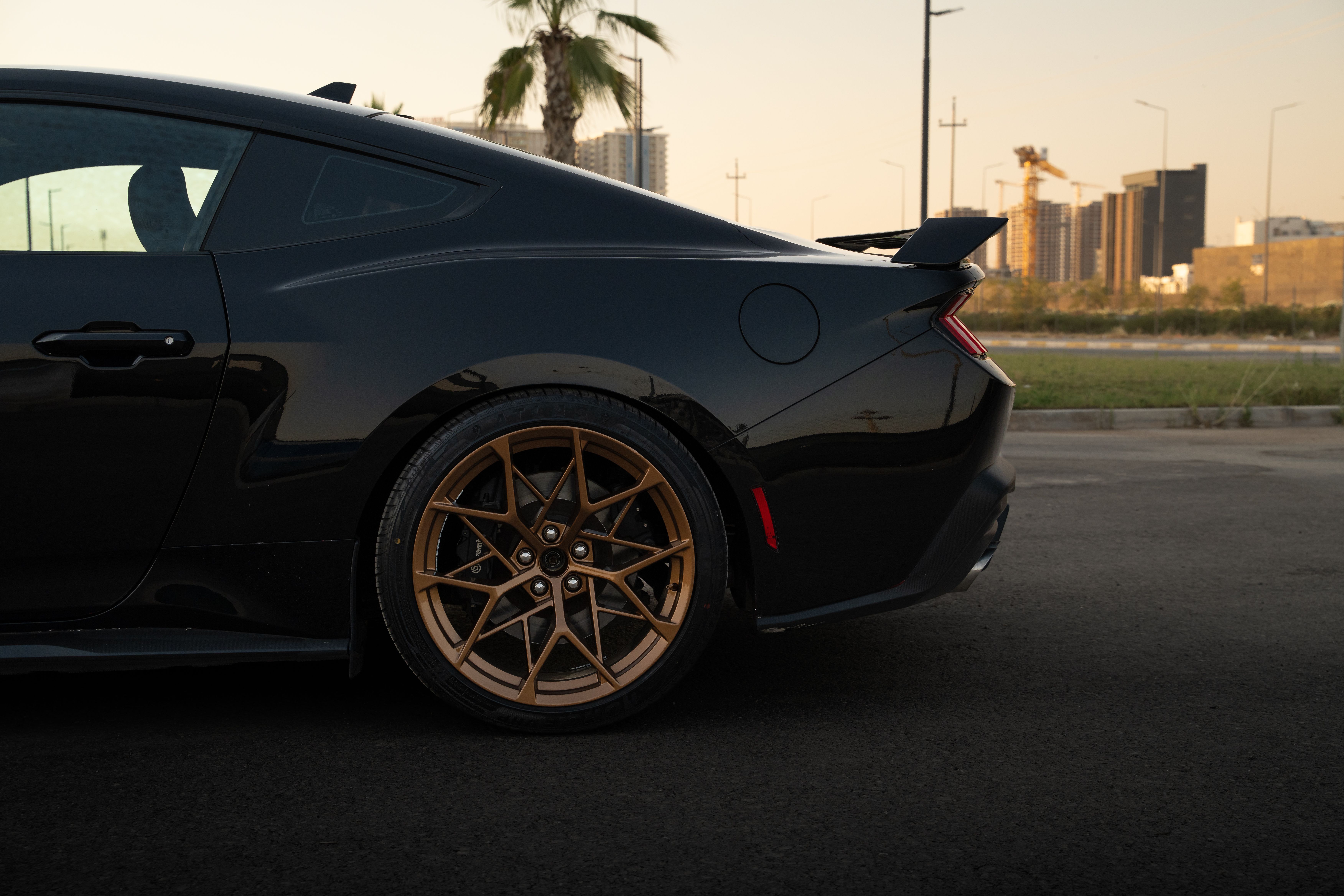 A stylish black sports car parked at sunset with city skyline in the background.