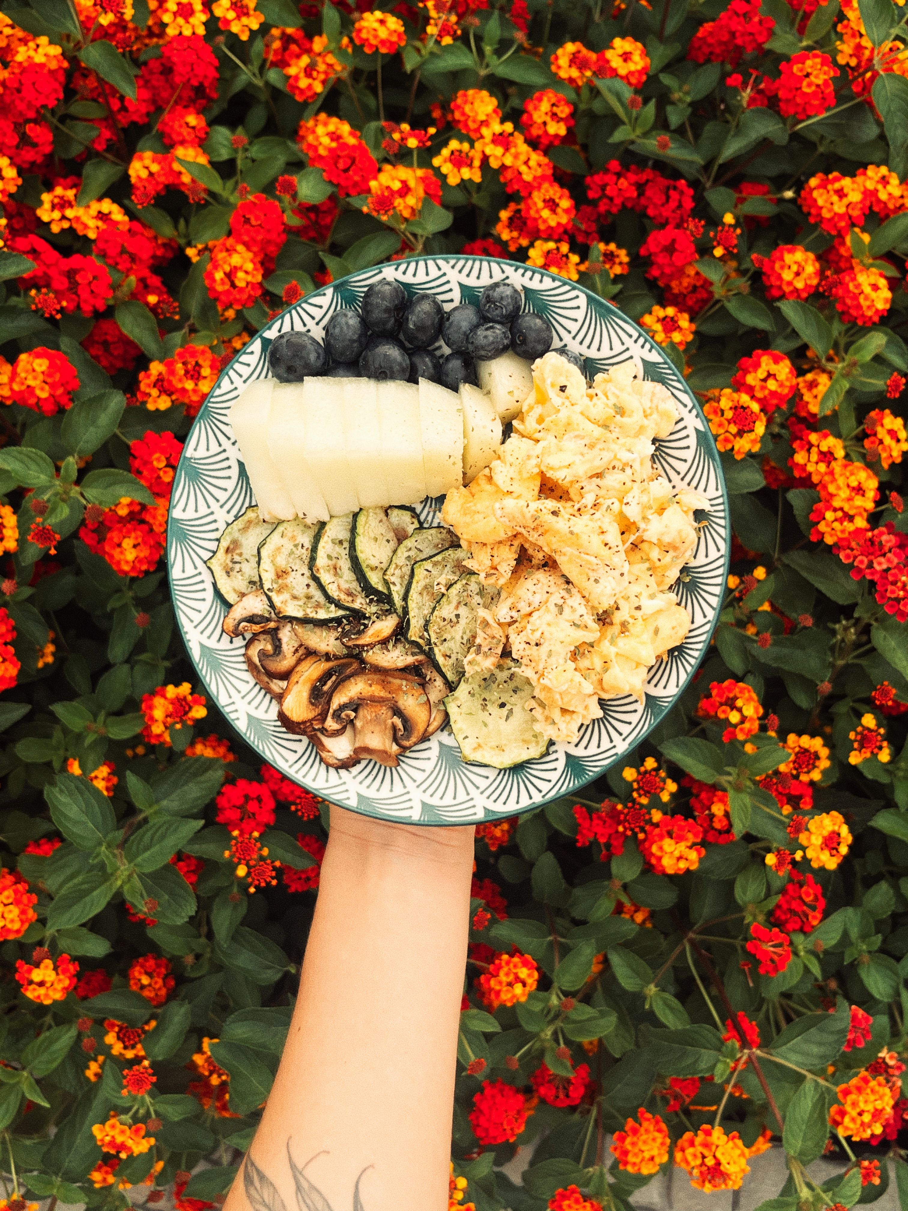 Colorful brunch plate with fruits and vegetables held over a floral backdrop, ideal for food photography.
