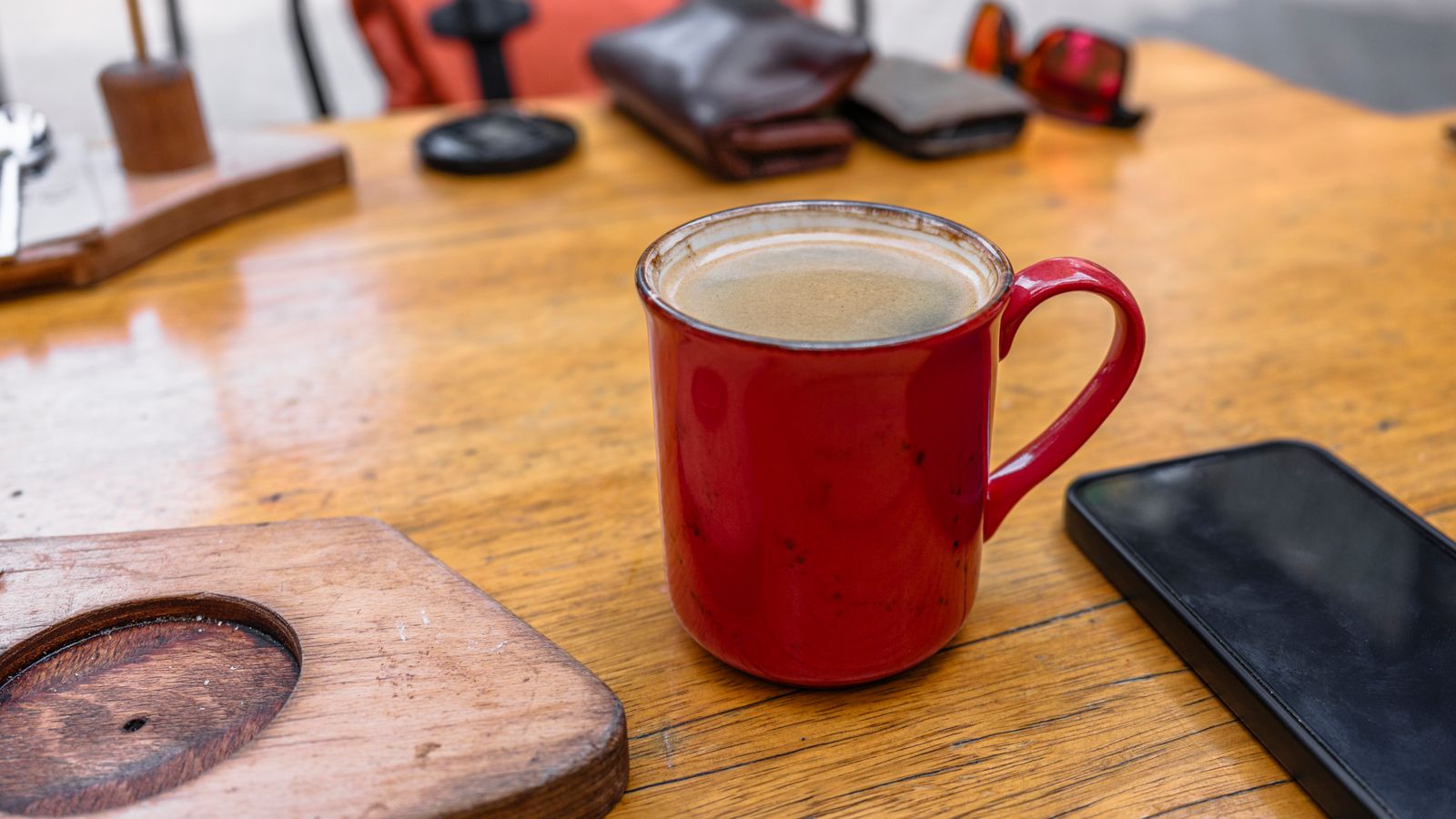 A cup of coffee next to a smartphone on a wooden table
