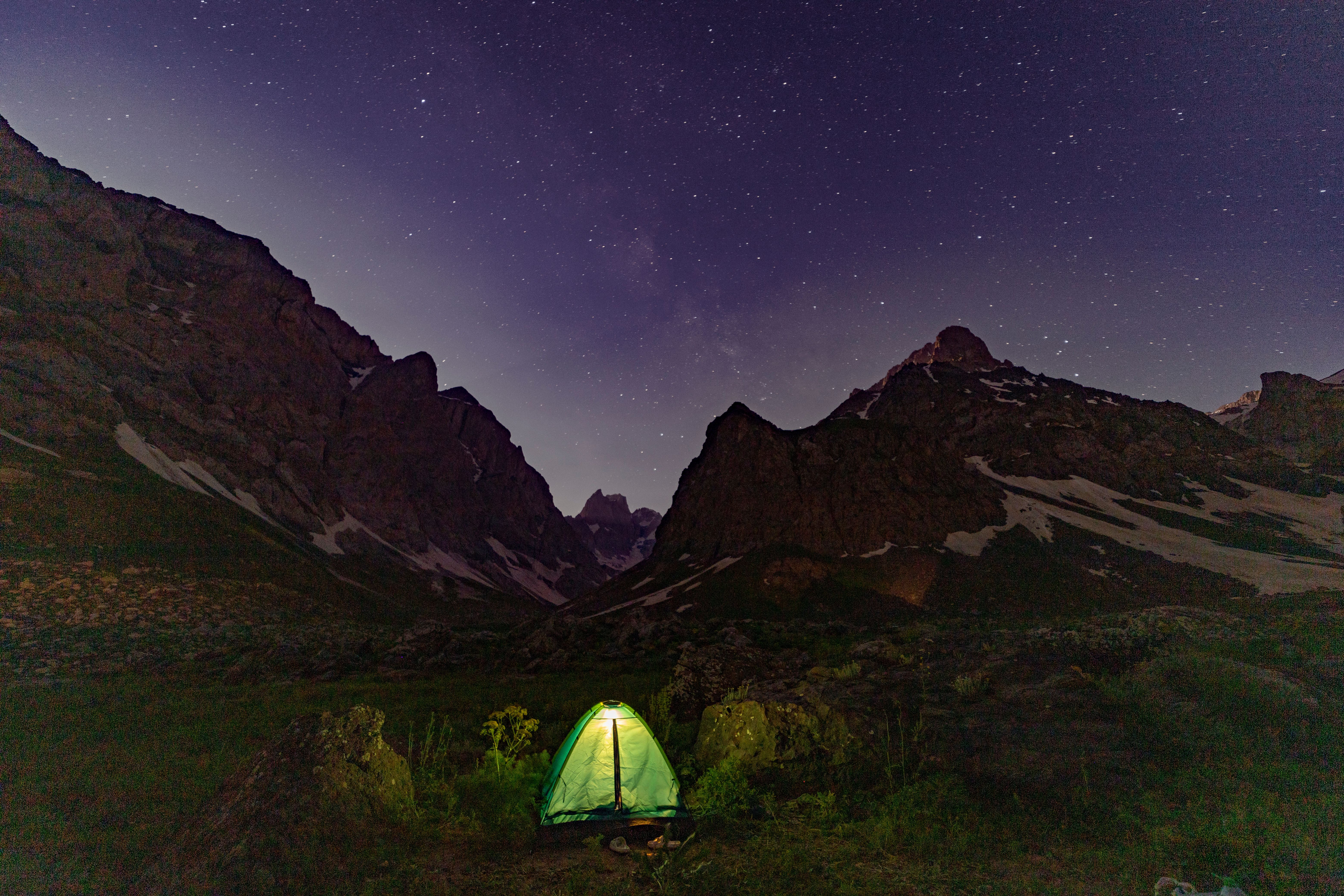 A glowing tent beneath starry mountain skies, perfect for night camping enthusiasts.