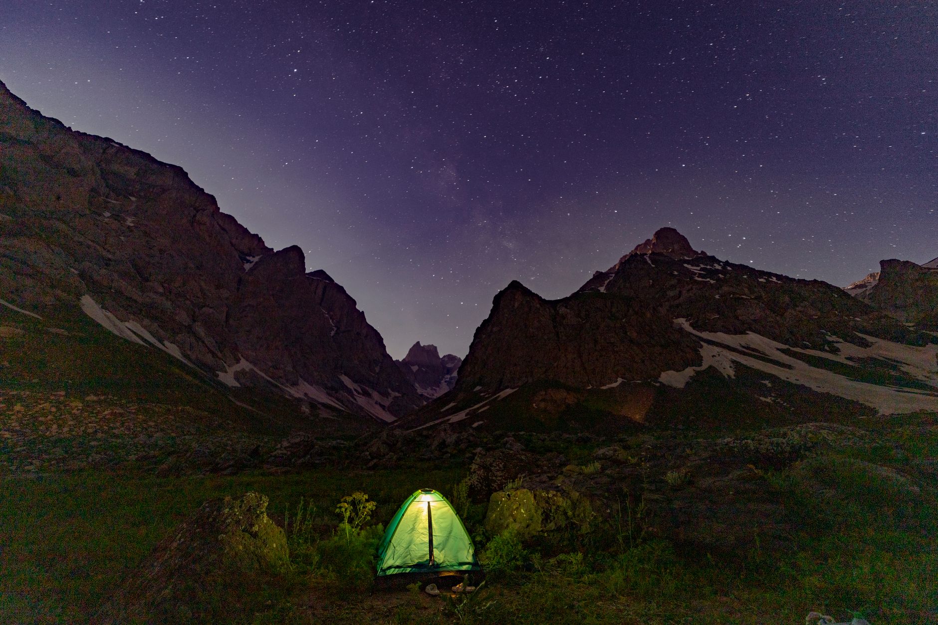 A glowing tent beneath starry mountain skies, perfect for night camping enthusiasts.