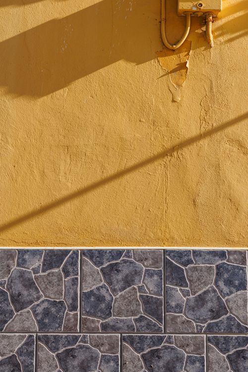 Free Yellow textured wall with contrasting stone tiles in Las Palmas, Spain. Warm tones and geometric design. Stock Photo