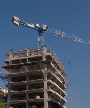 High-rise building under construction with a tower crane against clear blue skies in İzmir, Türkiye.