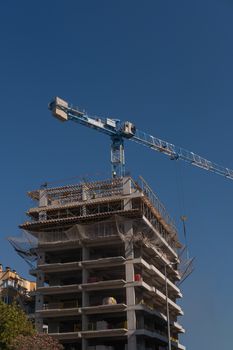 A tower crane works on high-rise building construction under a clear blue sky.