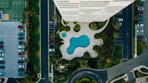 High-angle view of a swimming pool beside a tall urban building with surrounding parking lots.