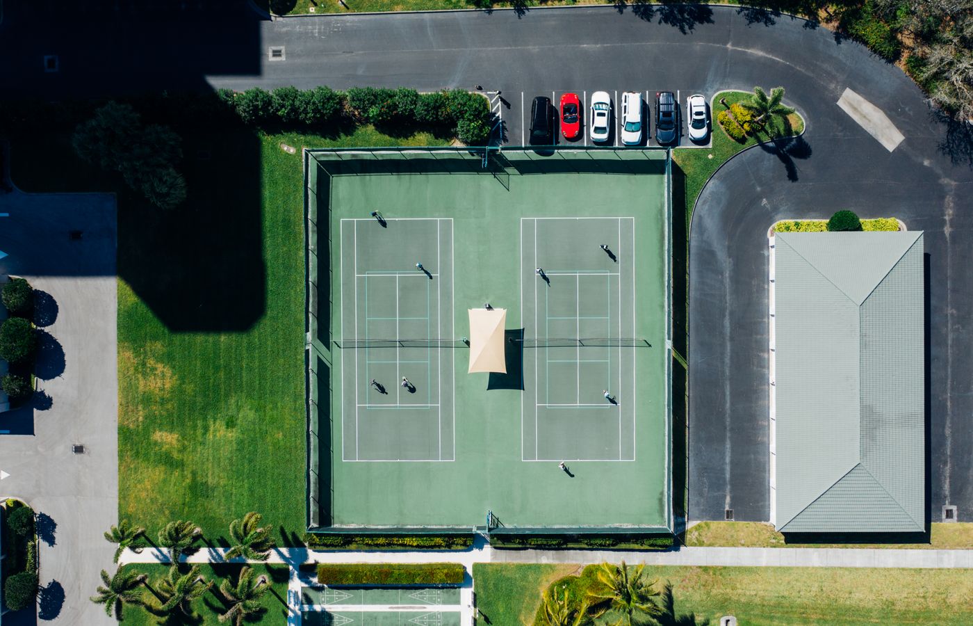 Drone shot showcasing tennis courts, parked cars, and residential area.