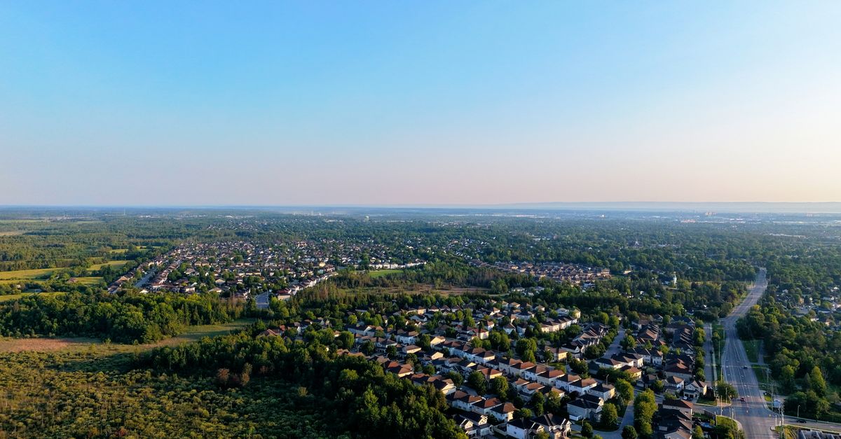 Aerial shot of suburbia next to a lush green forest under a clear blue sky.