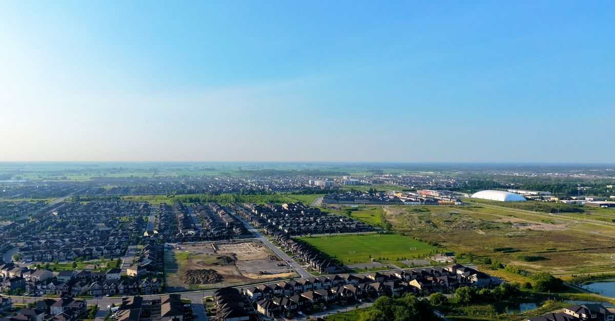 Aerial view showcasing suburban houses, green fields, and open sky.