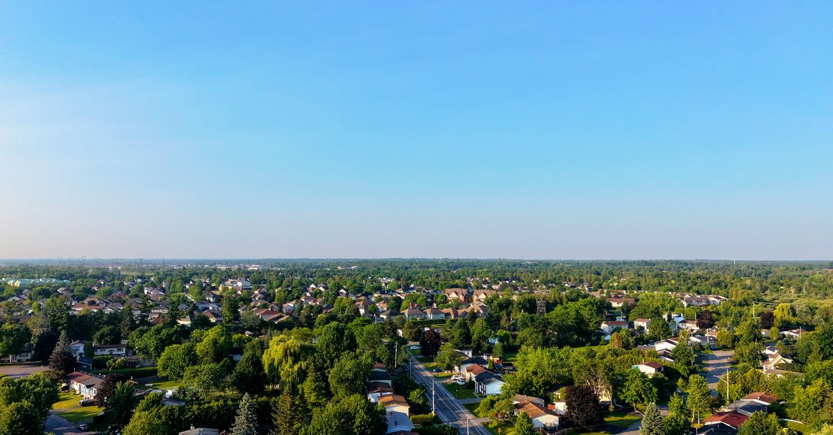 An expansive aerial view of a green suburban neighborhood under a clear blue sky.