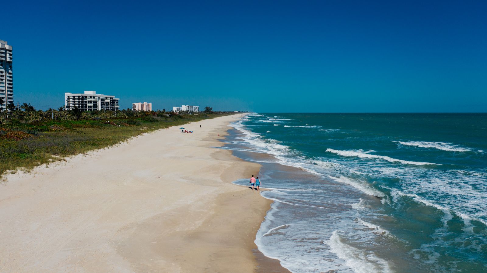 People on a sandy beach with waves and buildings in Florida
