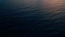 这是一张黄昏时分拍摄的航拍照片，展现了宁静的海景，其中黑暗的海浪更显静谧