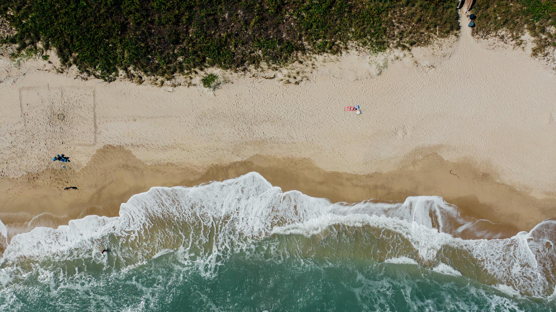 Aerial shot of a sandy beach with turquoise waves, capturing summer relaxation and coastal scenery.