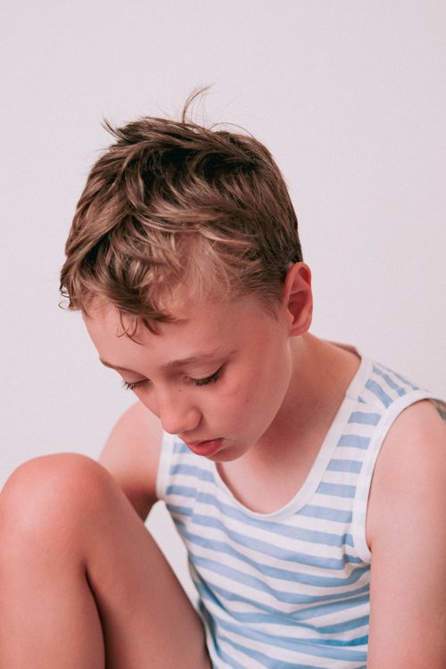 Free A thoughtful young boy in a striped tank top captured in a serene pose, looking down. Stock Photo