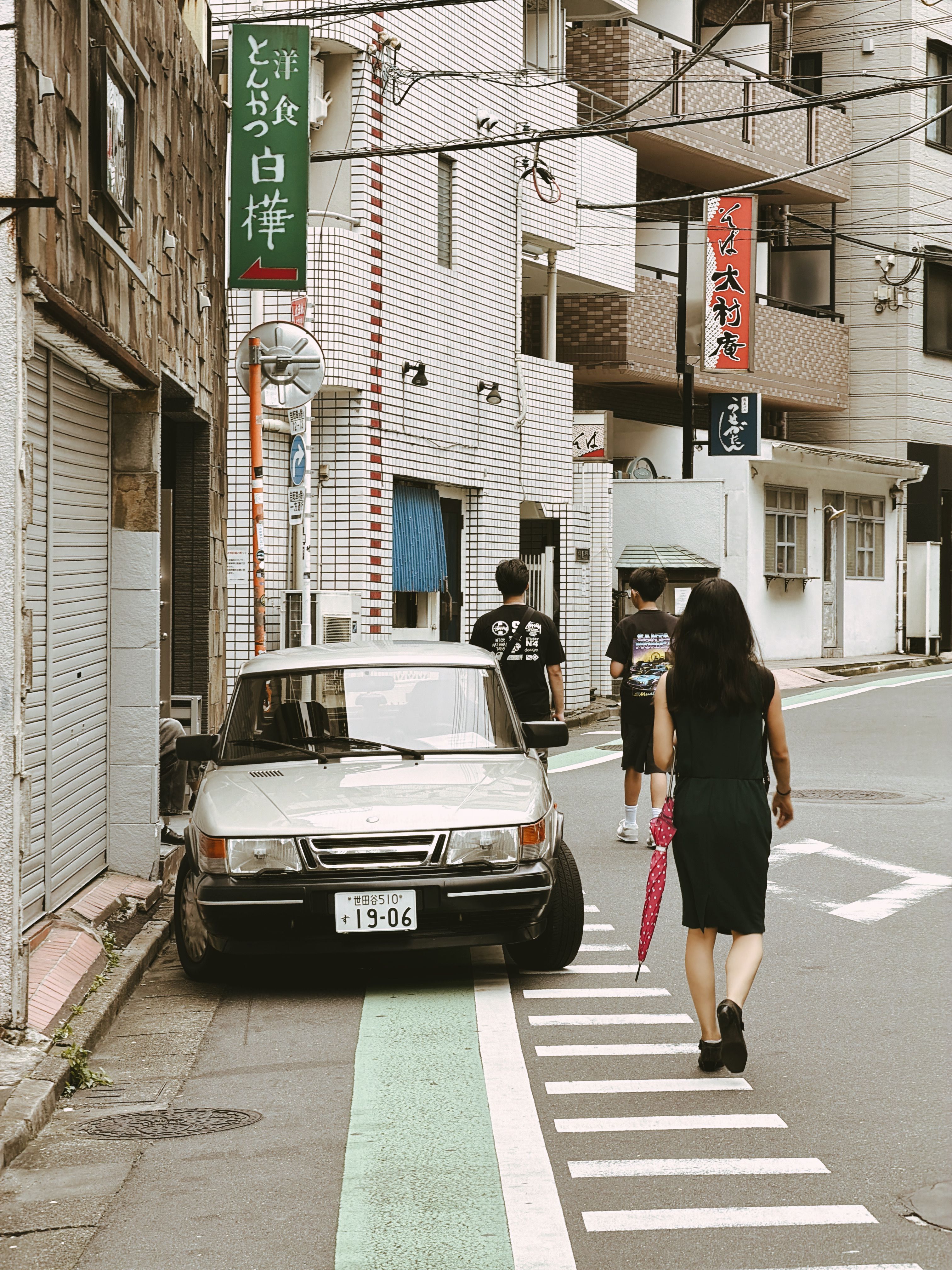 People walking by a vintage car on a vibrant Tokyo street with Japanese signage.