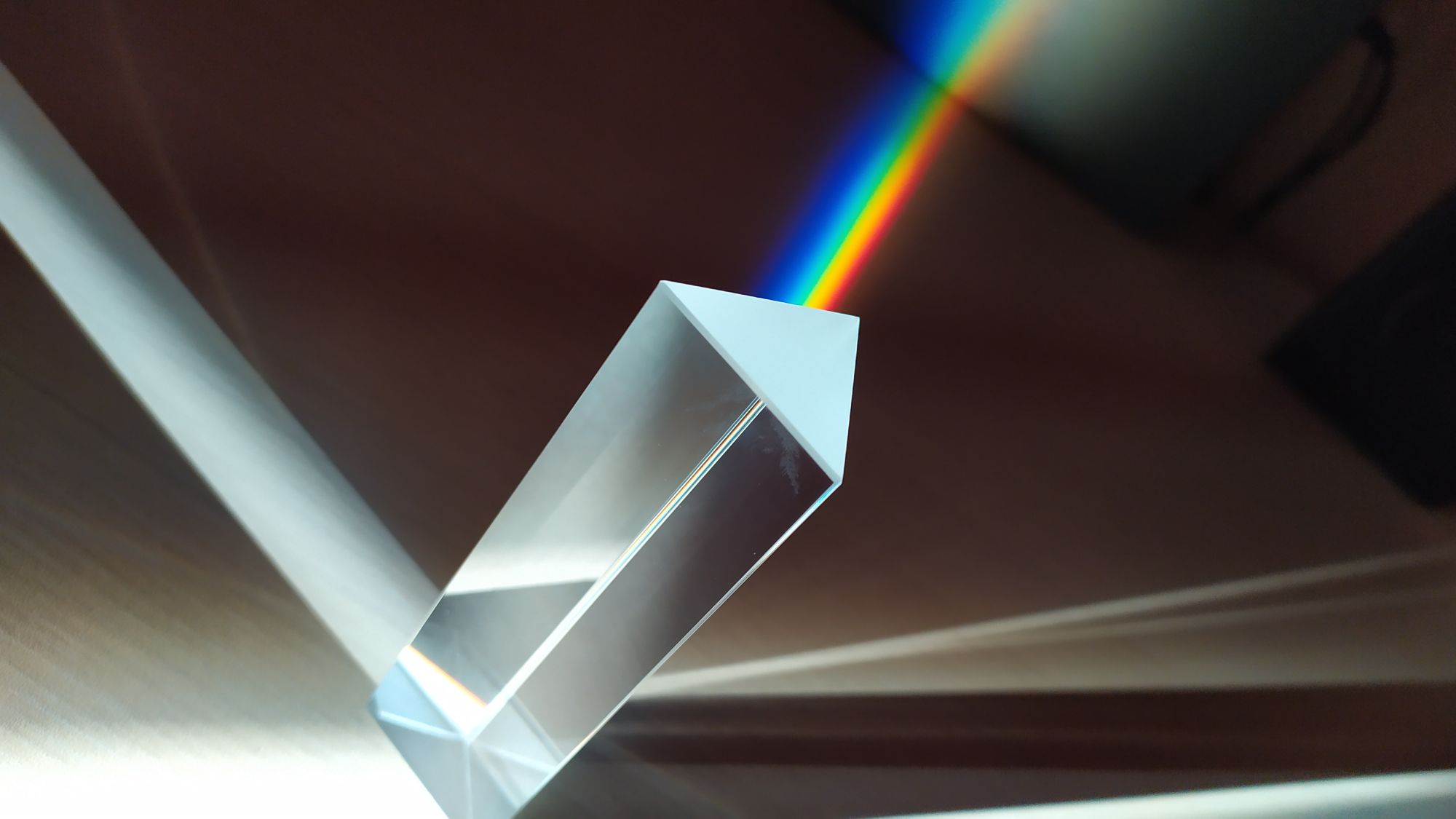 Haz de luz blanca atravesando un prisma de vidrio y separándose en una banda de colores sobre fondo oscuro