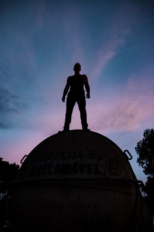 Free A silhouette of a man standing atop a structure during twilight with a colorful sky in the background. Stock Photo