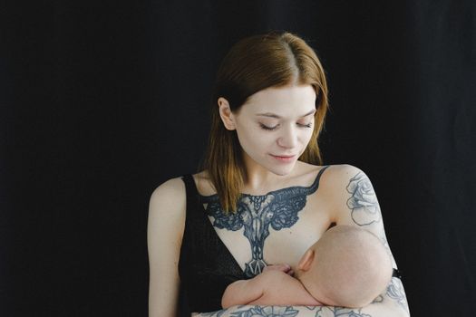 在黑暗背景下，一位有纹身的母亲正深情地母乳喂养她的婴儿