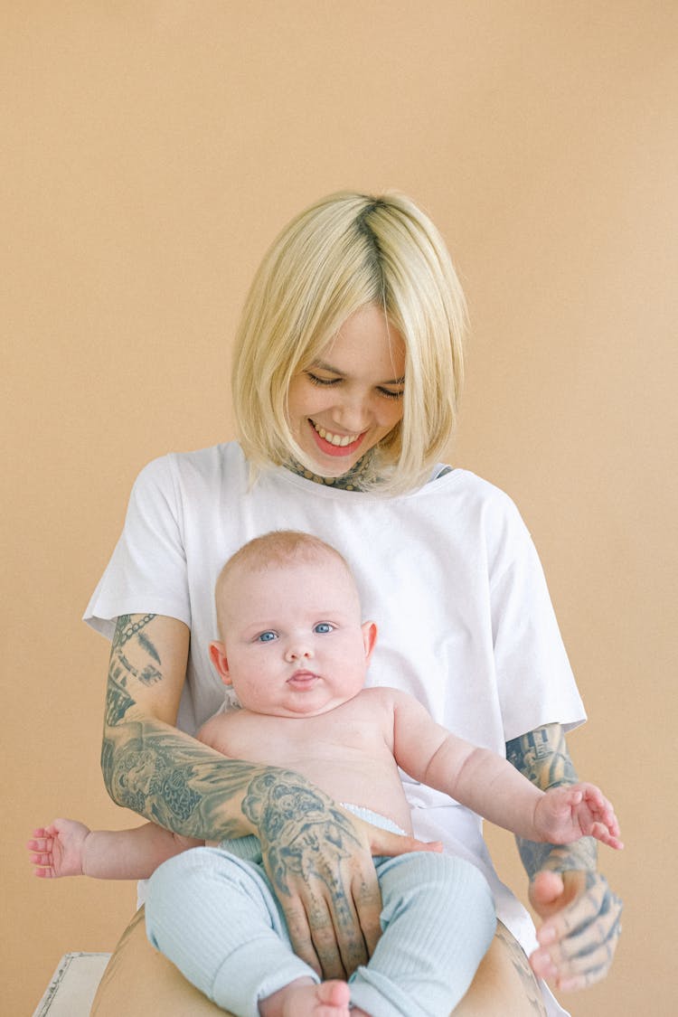 Happy Young Woman Holding Baby In Arms Against Beige Background In Studio